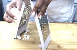 Person grating cheese on a wooden board with a stainless steel grater.